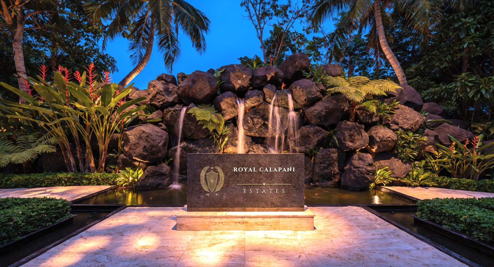Artist's impression of the estate entrance at dusk: water falling over stacked
            volcanic boulders behind a dark name stone reading Royal Calapani Estates.