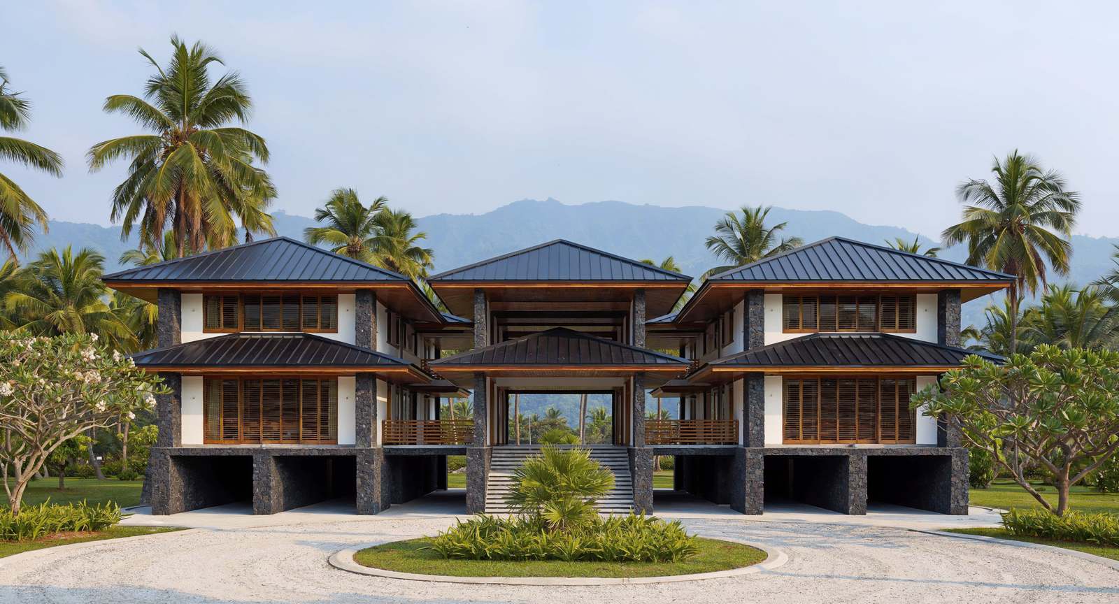 Artist's impression of the resort: three two-story pavilions on dark stone
            piers, joined by covered walkways, around an open-air entry reached from a
            circular drive.